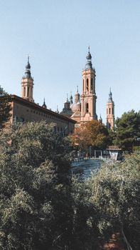 Majestic cathedral in Zaragoza surrounded by lush autumn foliage and clear skies.