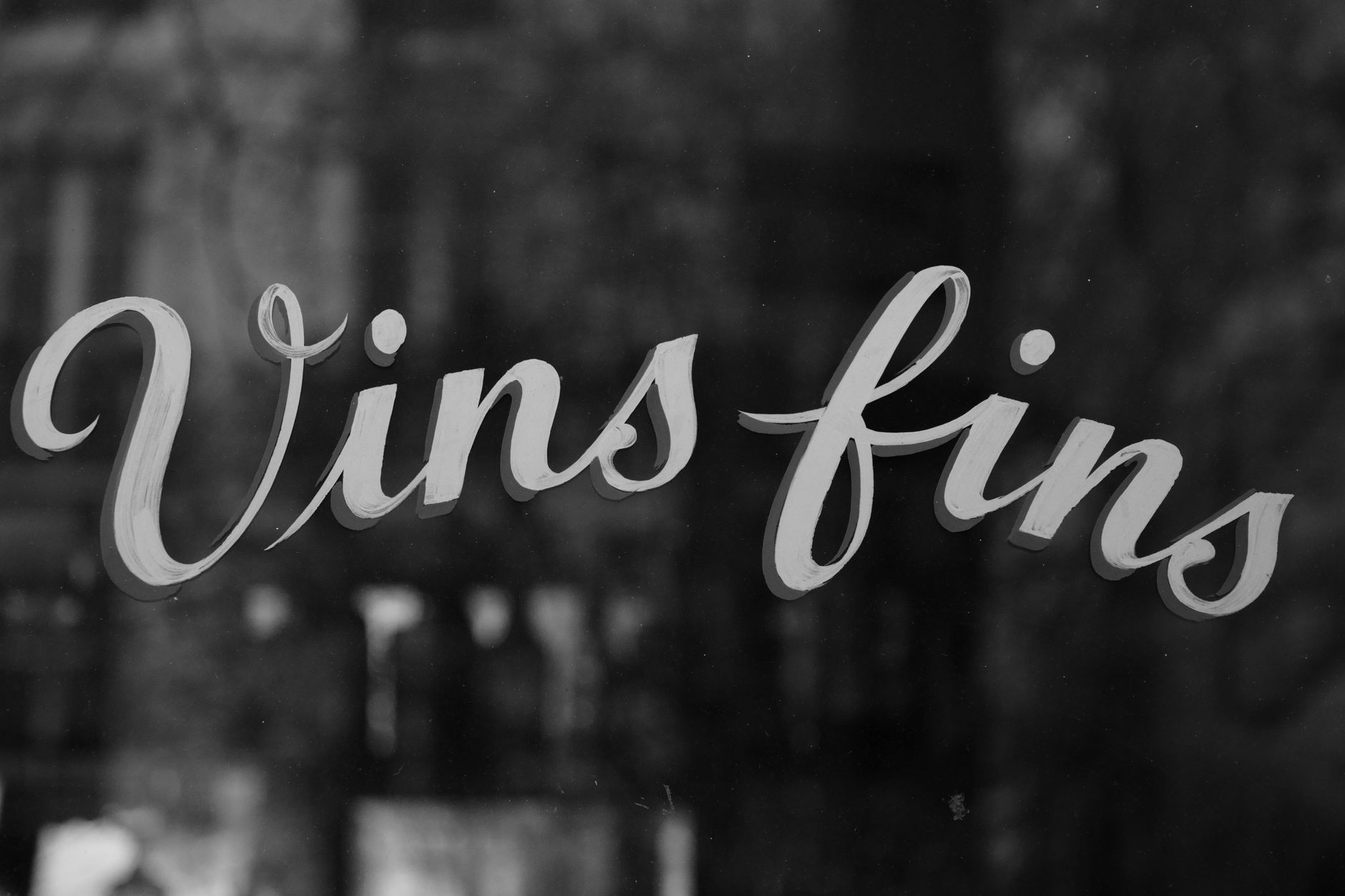 Black and white image of a cafe window in Paris with 'Vins fins' text, symbolizing fine wines.