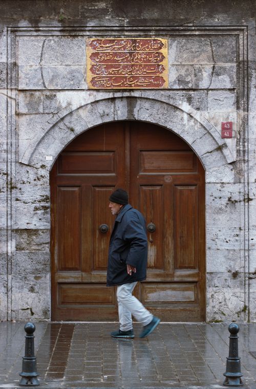 Free An elderly man walks by a historic wooden door under an arch on a rainy day. Stock Photo