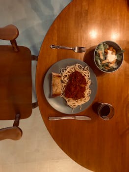 Aerial view of a dinner table set with spaghetti, salad, and a drink, perfect for food lovers.
