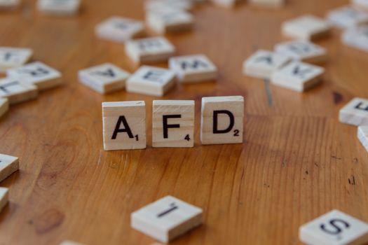 Close-up of scrabble tiles spelling 'AFD' on a wooden table surface, symbolizing political concepts.