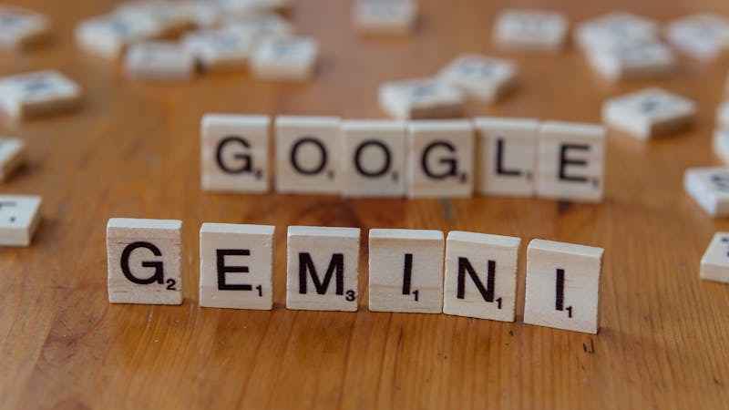 Scrabble tiles spelling out Google and Gemini on a wooden table, focusing on AI concepts.