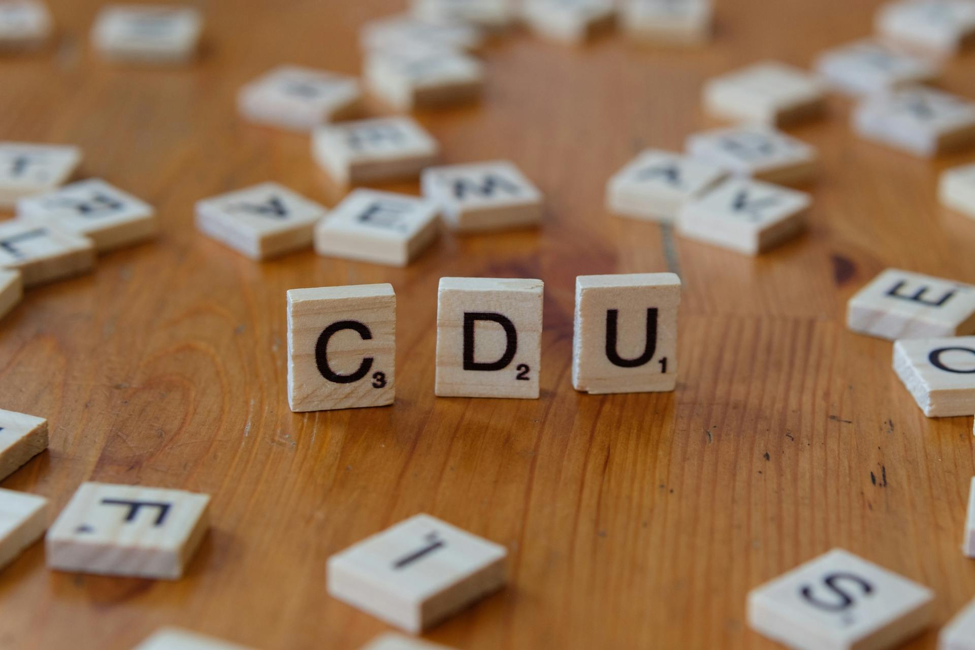 Scrabble tiles form the acronym CDU on a wooden table surface, symbolizing word games and political references.