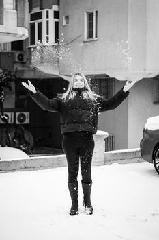 A woman joyfully throws snow in the air during a winter day in Istanbul, creating a playful scene.