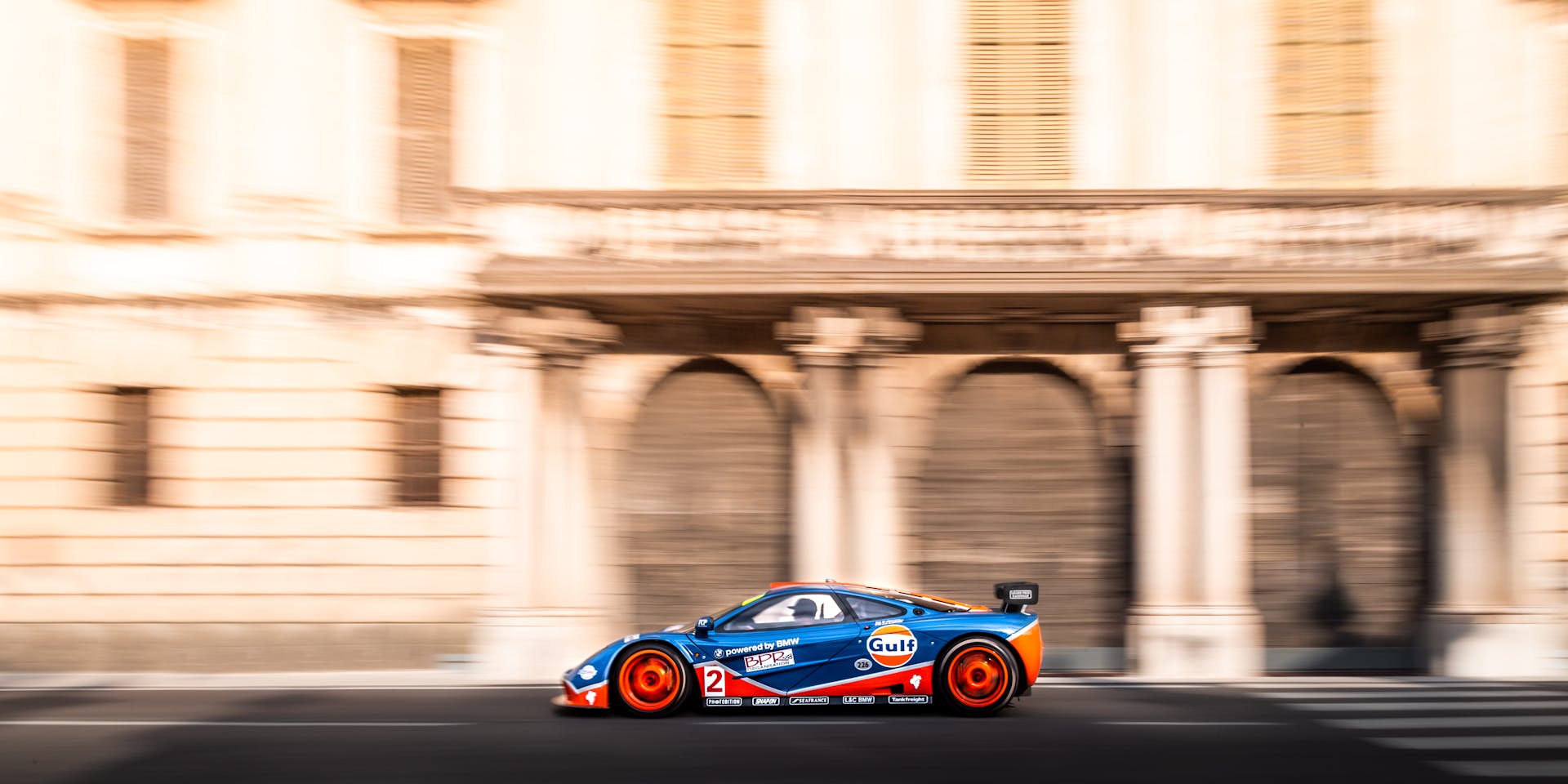 A vibrant racing car zooms by historic Italian architecture, showcasing speed and elegance.