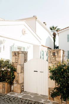 Quaint Mediterranean house entrance with a white gate, sunny ambiance.