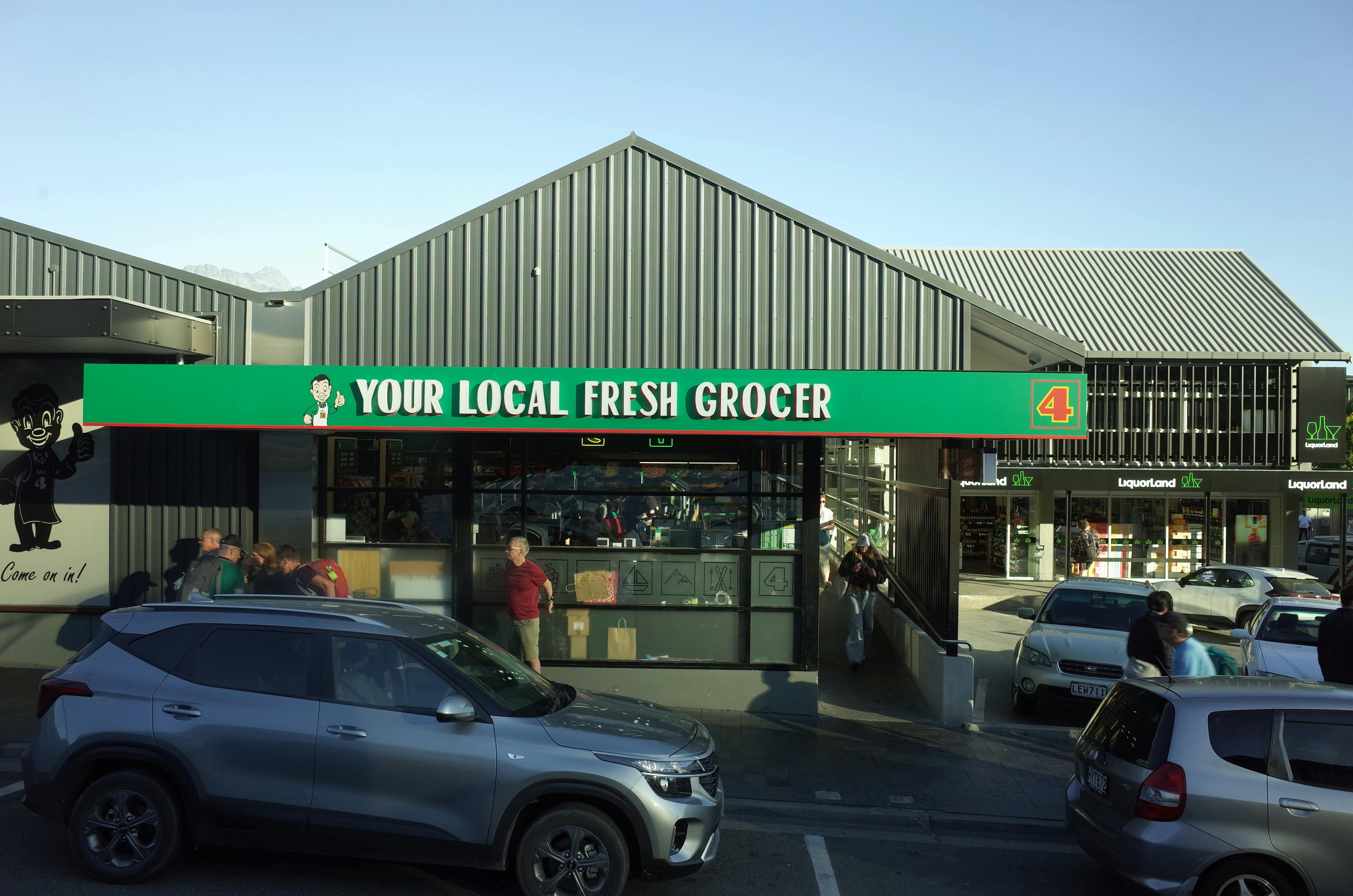 Daytime view of a local grocery store with parked cars and people.