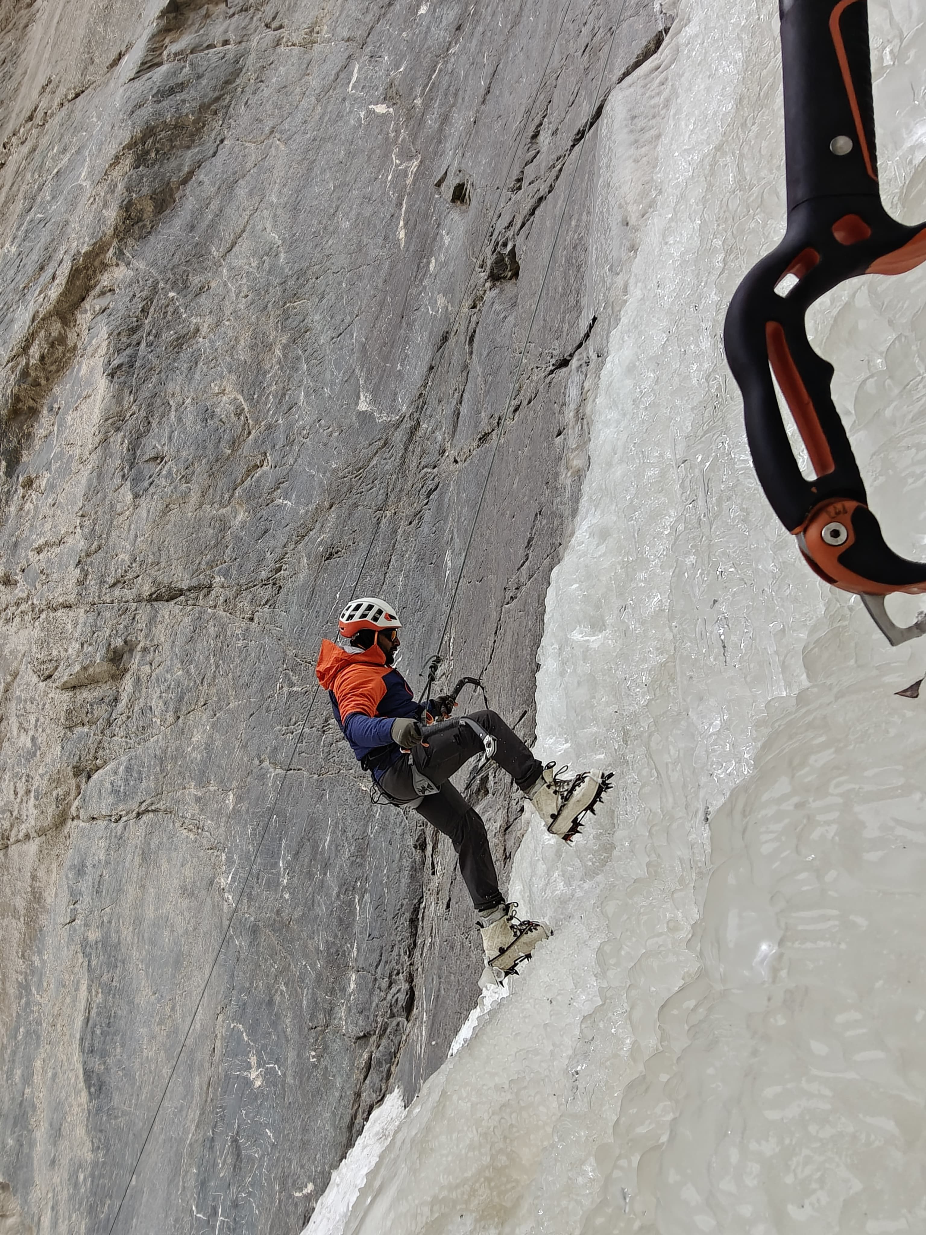 Ice climber ascending a frozen waterfall with gear in a dramatic winter setting.