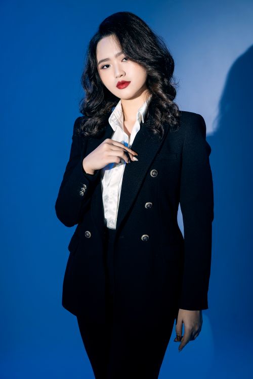 Free Elegant portrait of a woman in a black suit against a blue background, exuding confidence. Stock Photo