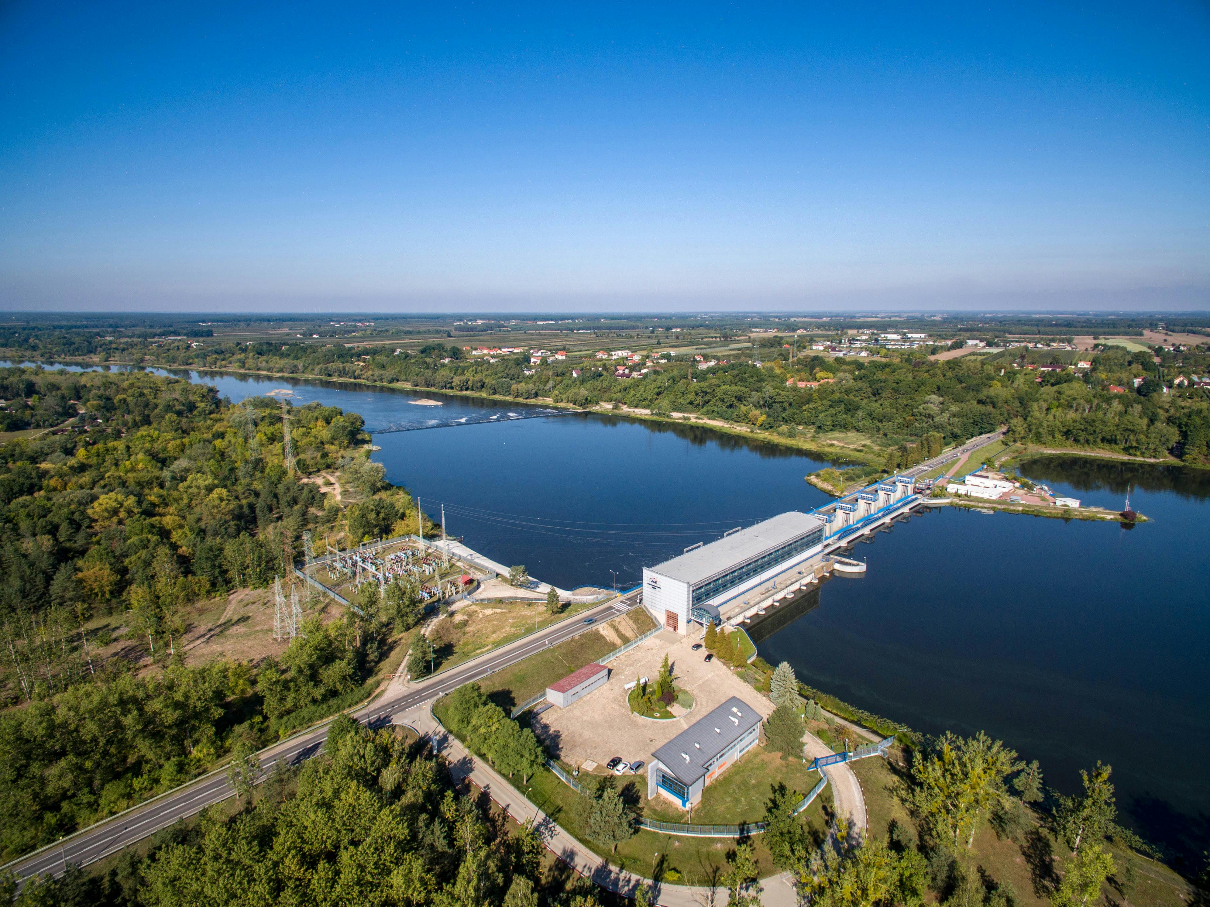 Scenic aerial view of a river dam surrounded by lush greenery under a clear sky.