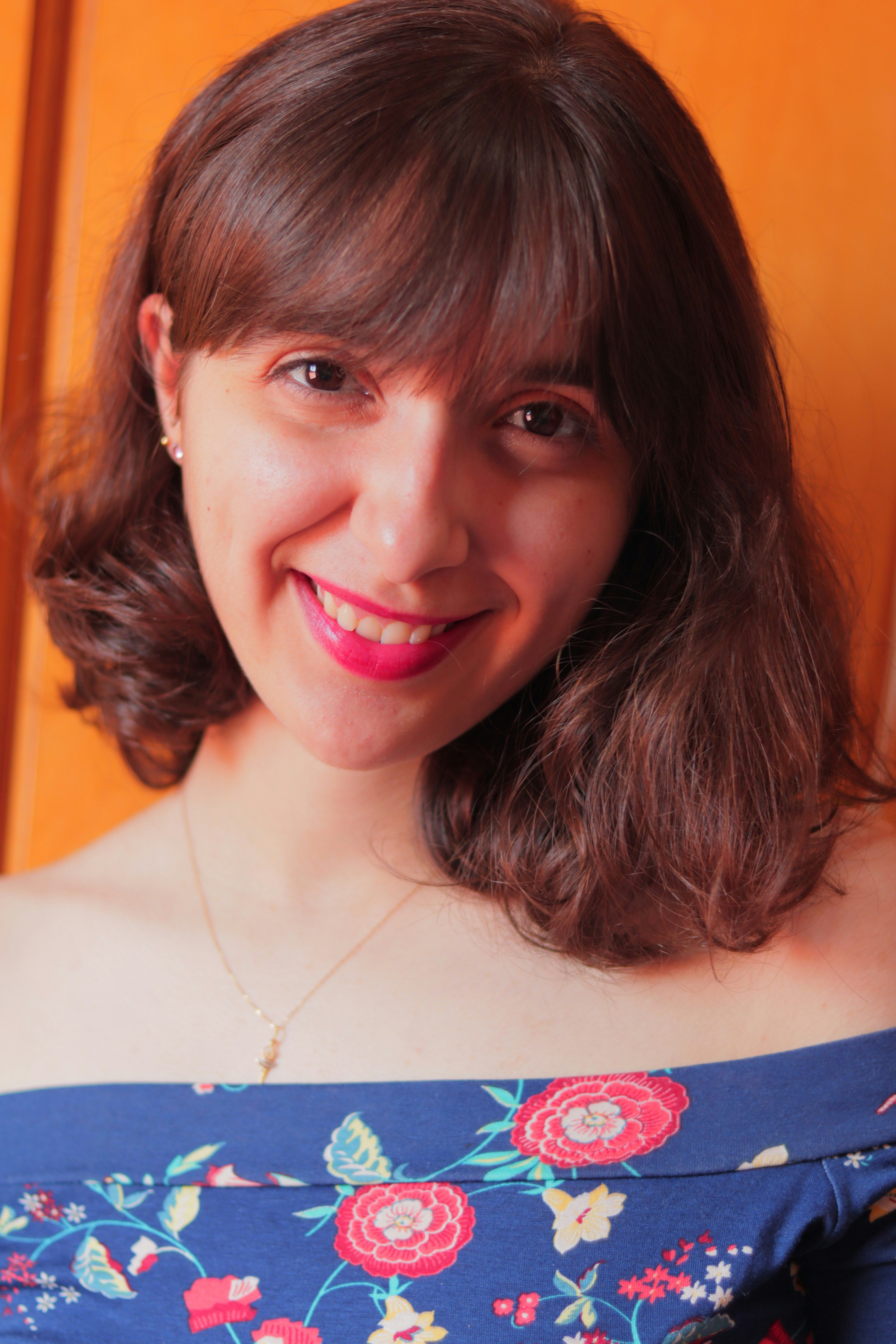 Portrait of a smiling woman with brown hair wearing a floral off-shoulder top.