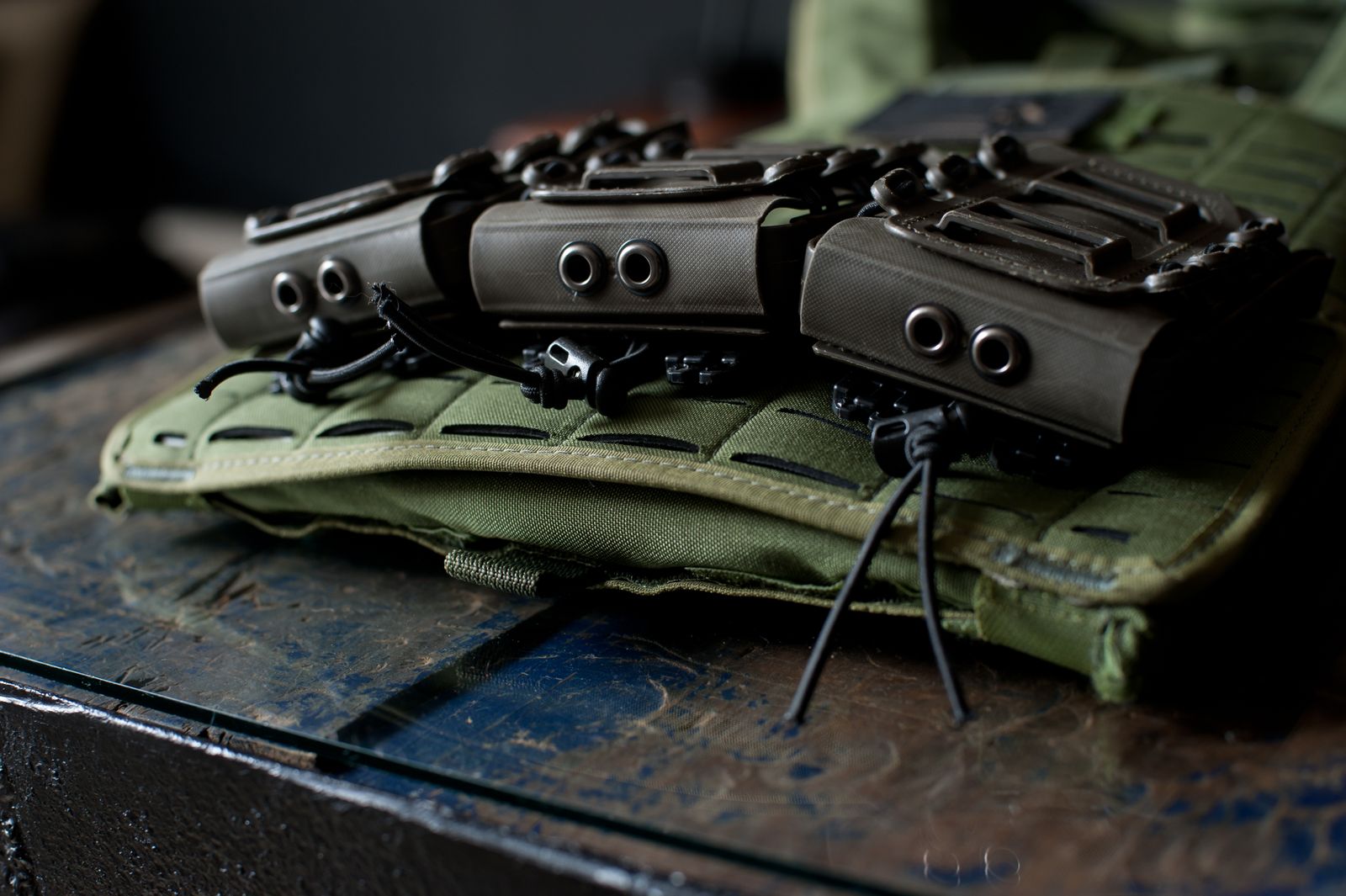 Close-up of MOLLE modular webbing rows on a green tactical vest with pouches attached, showing the standard PALS grid spacing.