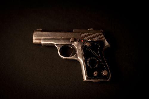 Free Close-up of a vintage pistol on a dark surface, showcasing intricate details and metallic finish. Stock Photo