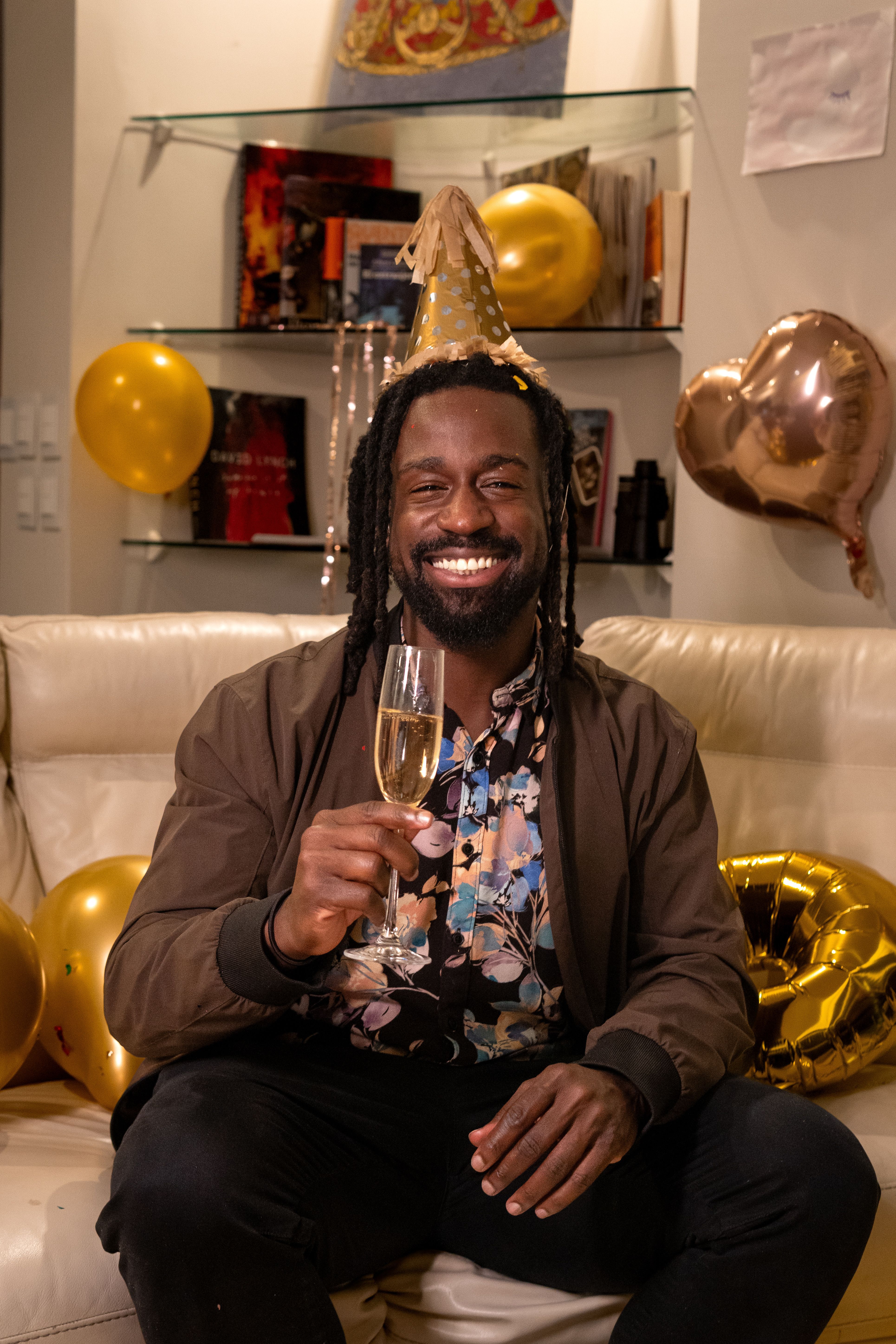 Man celebrating a birthday with a champagne toast, surrounded by party decor and balloons.