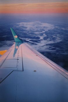 Scenic airplane wing view over clouds during sunset, creating a colorful, serene atmosphere.