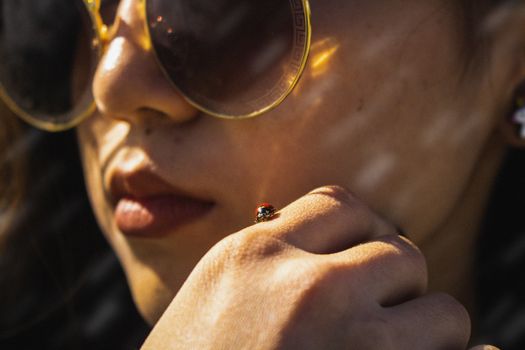 特写一个女人在户外温暖的灯光下，戴着太阳镜，手上停着一只瓢虫