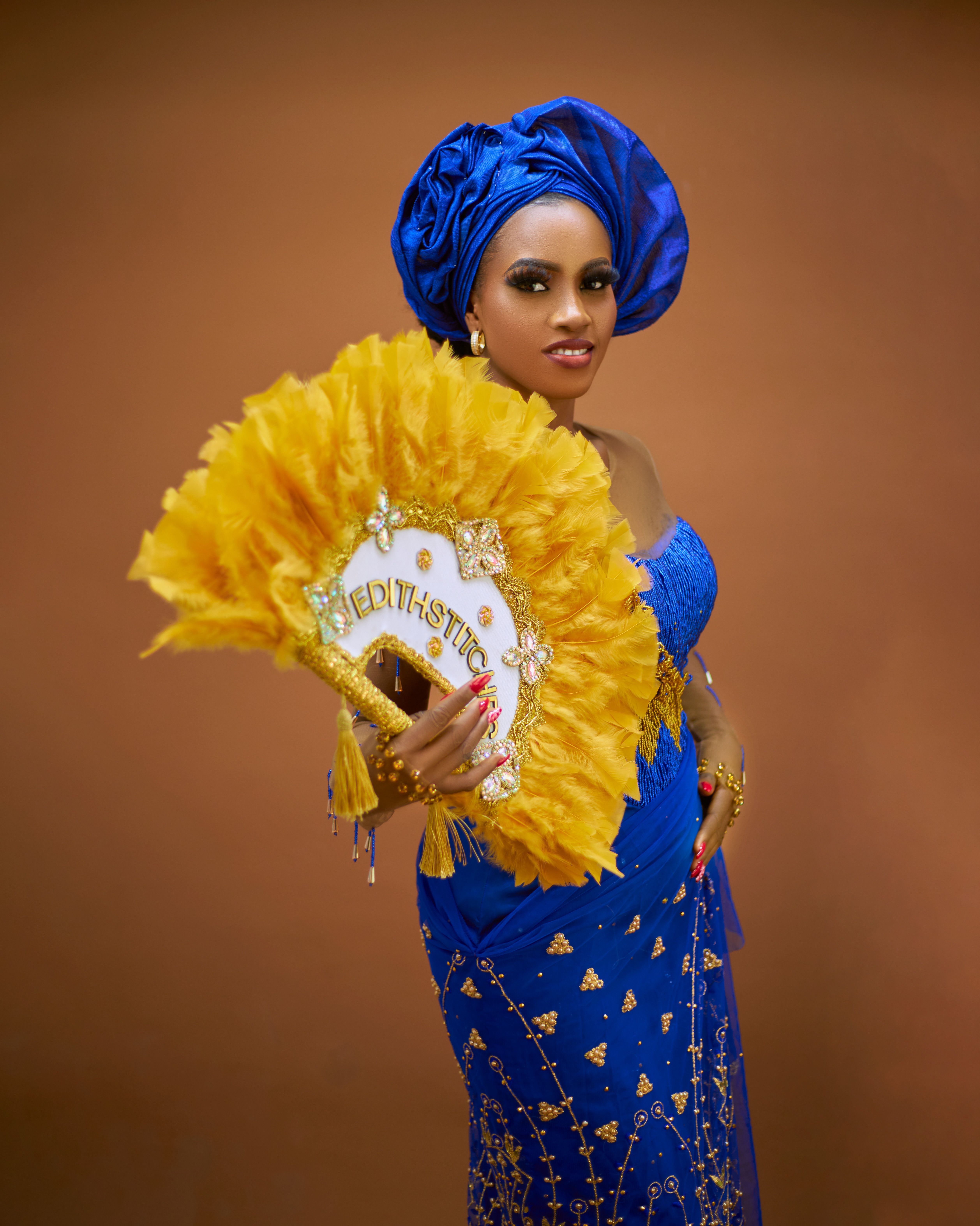 Beautiful woman in blue and yellow traditional African attire holding a decorative fan.