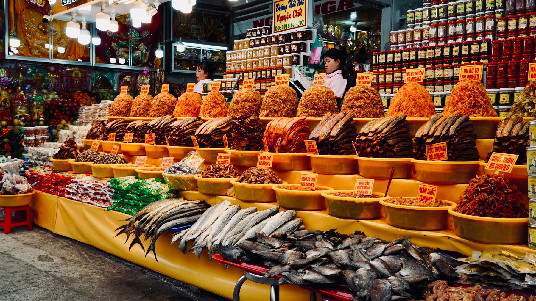 Colorful assortment of dried goods and fresh fish at a bustling Vietnamese market stall.