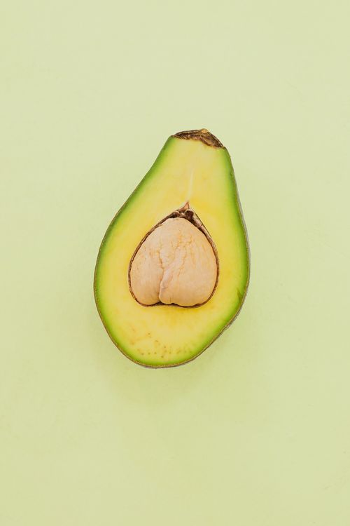Free A single avocado half with seed on a light pastel backdrop. Perfect for food-related designs. Stock Photo