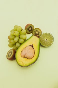 Vibrant fresh avocado, kiwi, lime, and grapes on a pastel green background. Ideal for food concepts.