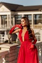 一位穿着惊艳红色礼服的时尚女性自信地站在阳光明媚的露台上