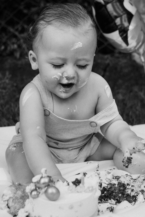 Free Black and white portrait of a baby in overalls enjoying a messy outdoor cake smash. Stock Photo