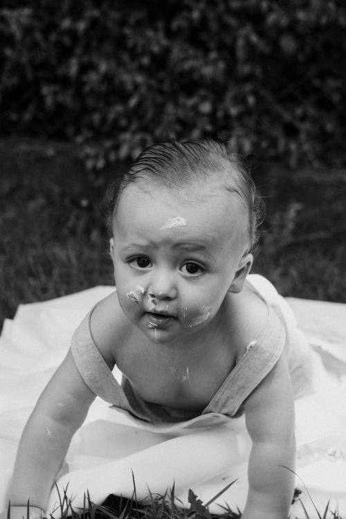 Free Black and white photo of a baby enjoying a cake smash outdoors, displaying playful curiosity. Stock Photo