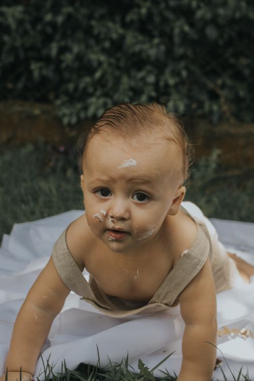 Free Cute baby covered in cake frosting crawling on a blanket outdoors. Stock Photo