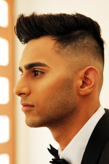 Profile portrait of a young man with a sharp hairstyle wearing a suit indoors.