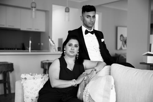 Stylish couple in formal wear, relaxed in a modern living room setting.