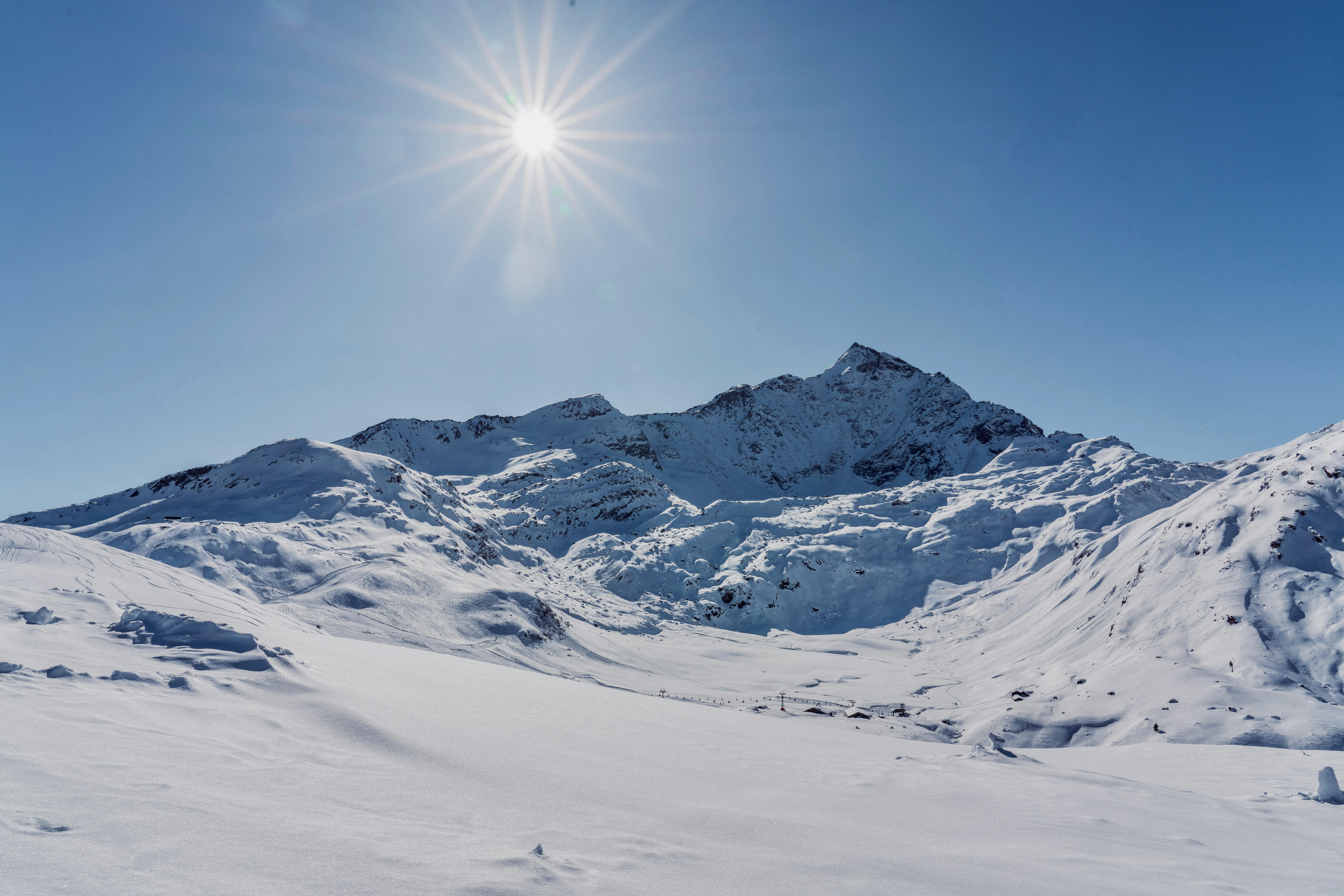A majestic snowy mountain landscape under a bright sun, featuring pristine white snow and clear blue sky.