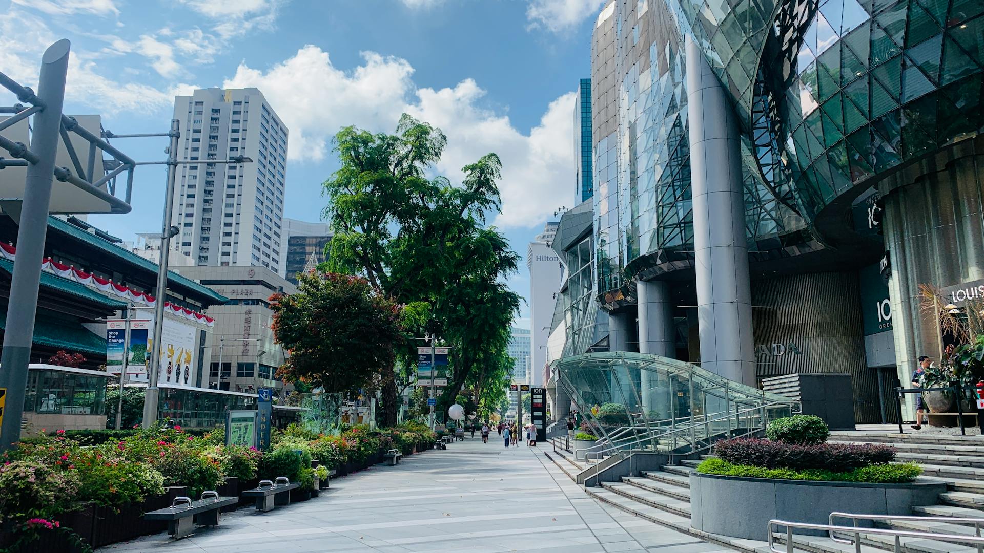 A vibrant street in Singapore featuring modern skyscrapers, lush greenery, and clear blue skies.