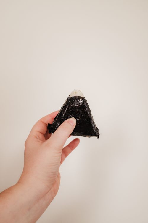 Free Close-up of a hand holding a traditional Japanese onigiri with seaweed Stock Photo