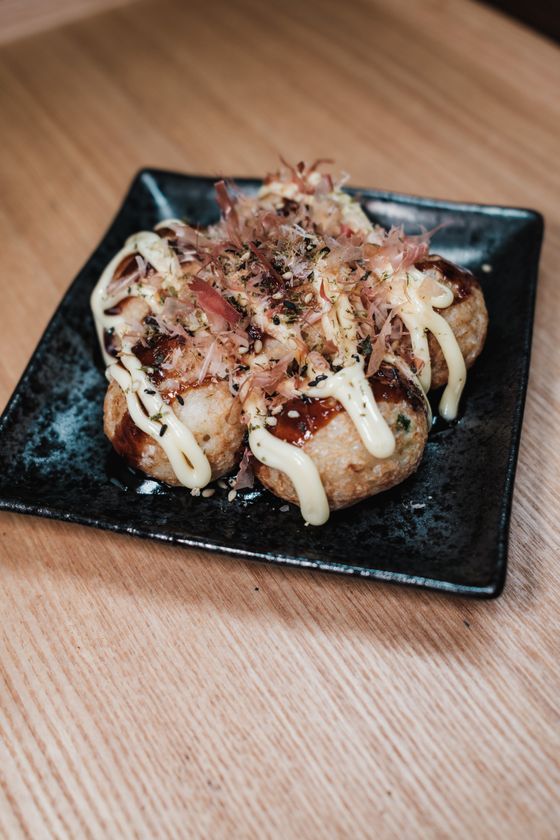 Takoyaki balls with brown sauce, mayonnaise drizzle, bonito flakes and seaweed on a black plate