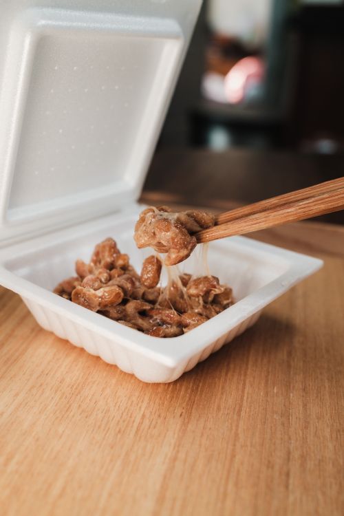 Free Chopsticks lifting sticky fermented soybeans from a white container, typical in Japanese cuisine. Stock Photo
