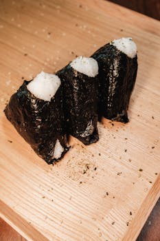 Three delicious Japanese onigiri rice balls wrapped in seaweed on a wooden board.
