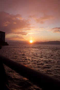 A beautiful sunset casting warm hues over calm ocean waters and distant hills.