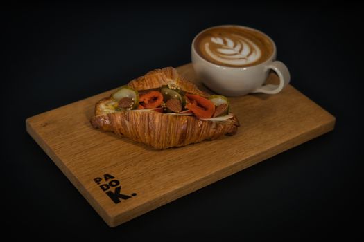 Delicious croissant filled with vegetables, served with latte art coffee on a wooden board.
