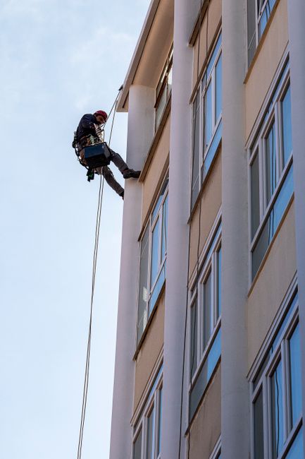 A professional window cleaner performs abseiling on a tall building facade in daylight.