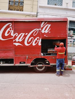 A worker unloads bottles from a Coca-Cola delivery truck on a city street.