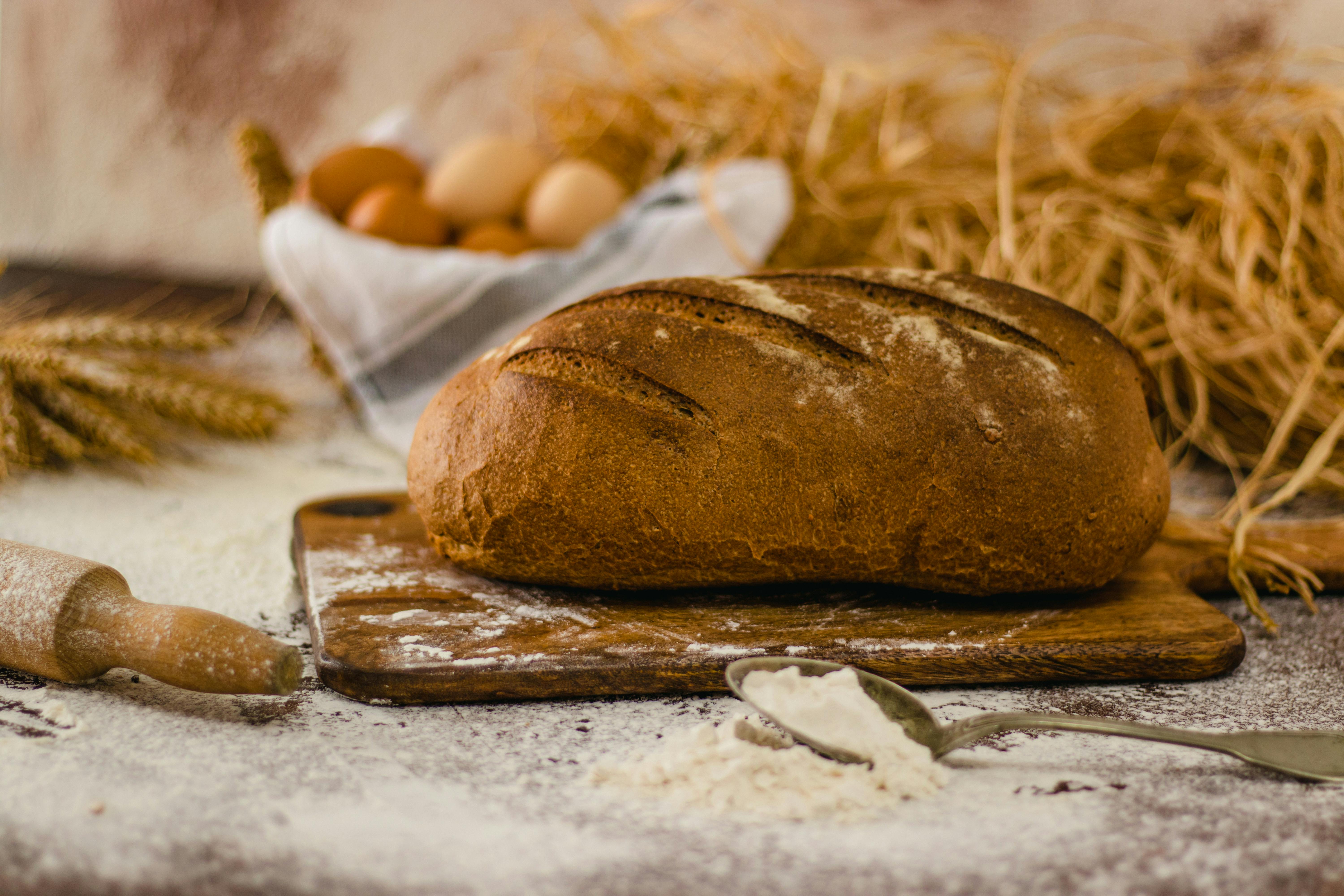 A loaf of freshly baked rustic bread on a wooden cutting board with baking ingredients around.