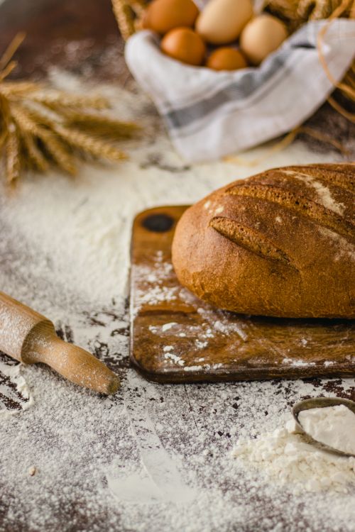 Free A rustic loaf of bread on a floured table with eggs and wheat, showcasing traditional baking. Stock Photo