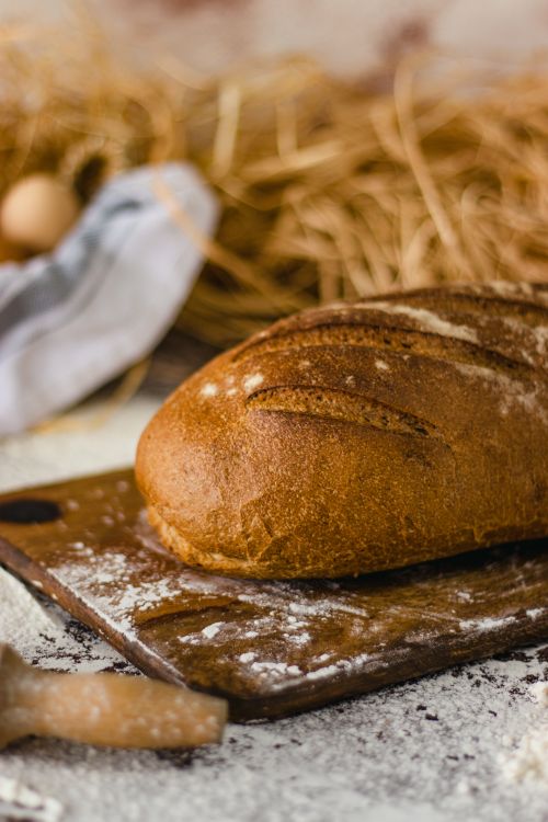 Free Close-up of a freshly baked loaf of bread on a rustic wooden board with a straw background. Stock Photo