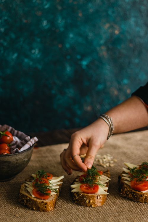Free A hand garnishing sandwiches with fresh tomatoes and herbs on whole grain bread. Stock Photo