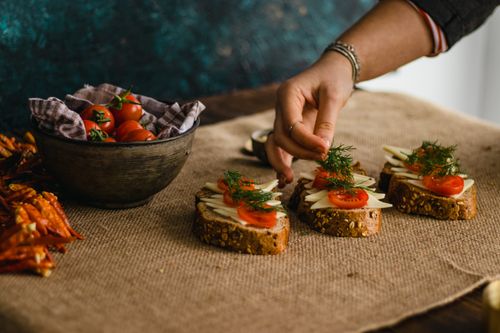Free Close-up of a hand preparing artisan multigrain sandwiches with cheese and tomatoes. Stock Photo