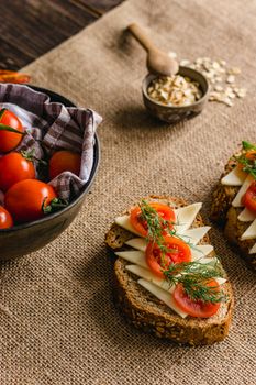 Slices of multigrain bread topped with cheese and tomatoes on burlap with fresh cherry tomatoes nearby.