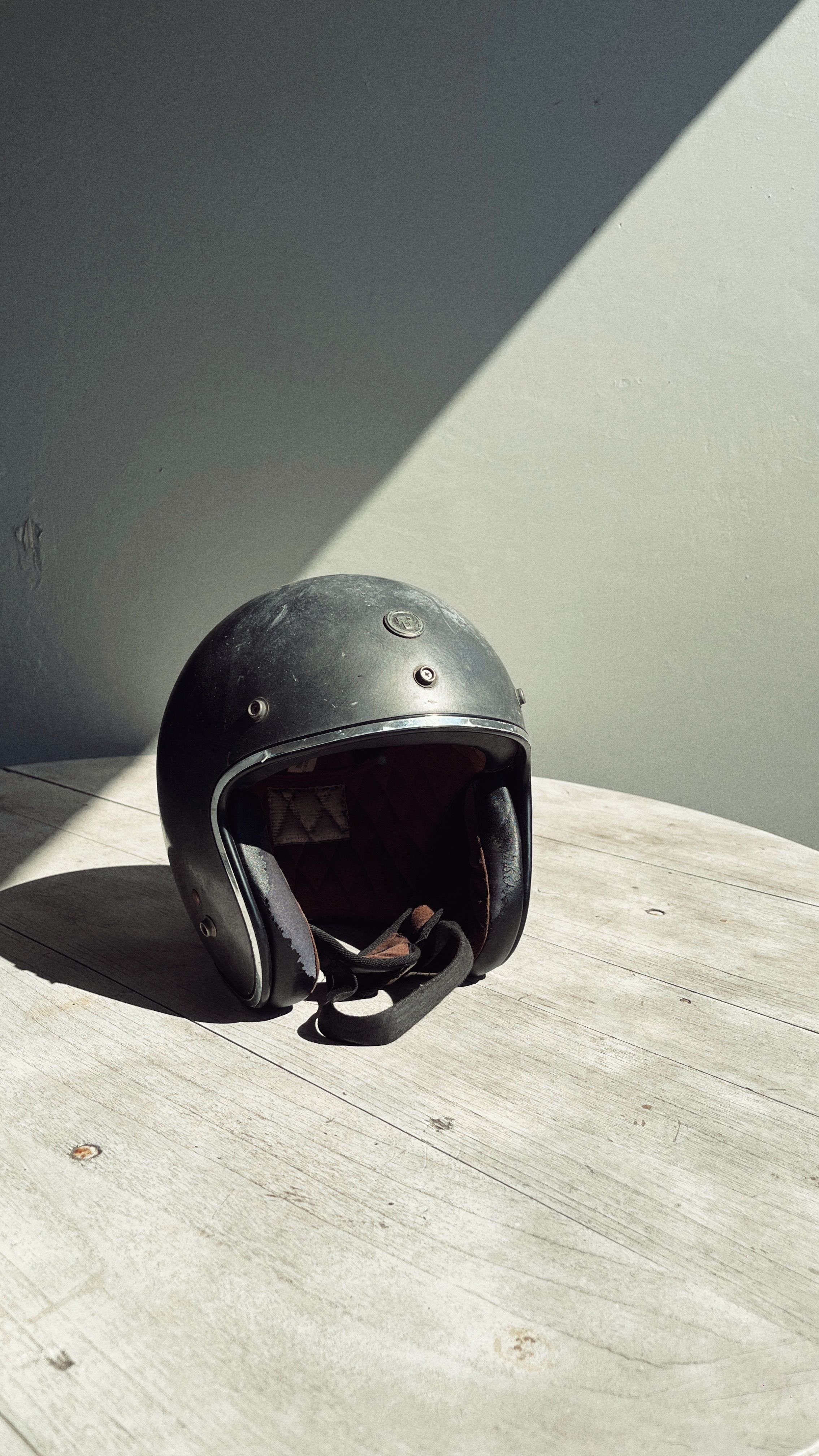 Casque moto vintage ouvert de type jet, posé sur un tabouret en bois