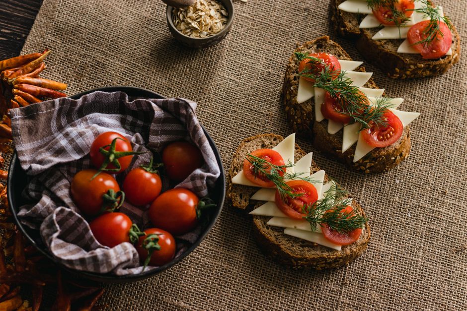 A rustic arrangement of multi-grain bread with sliced cheese, tomatoes, and dill on burlap, perfect for culinary themes.
