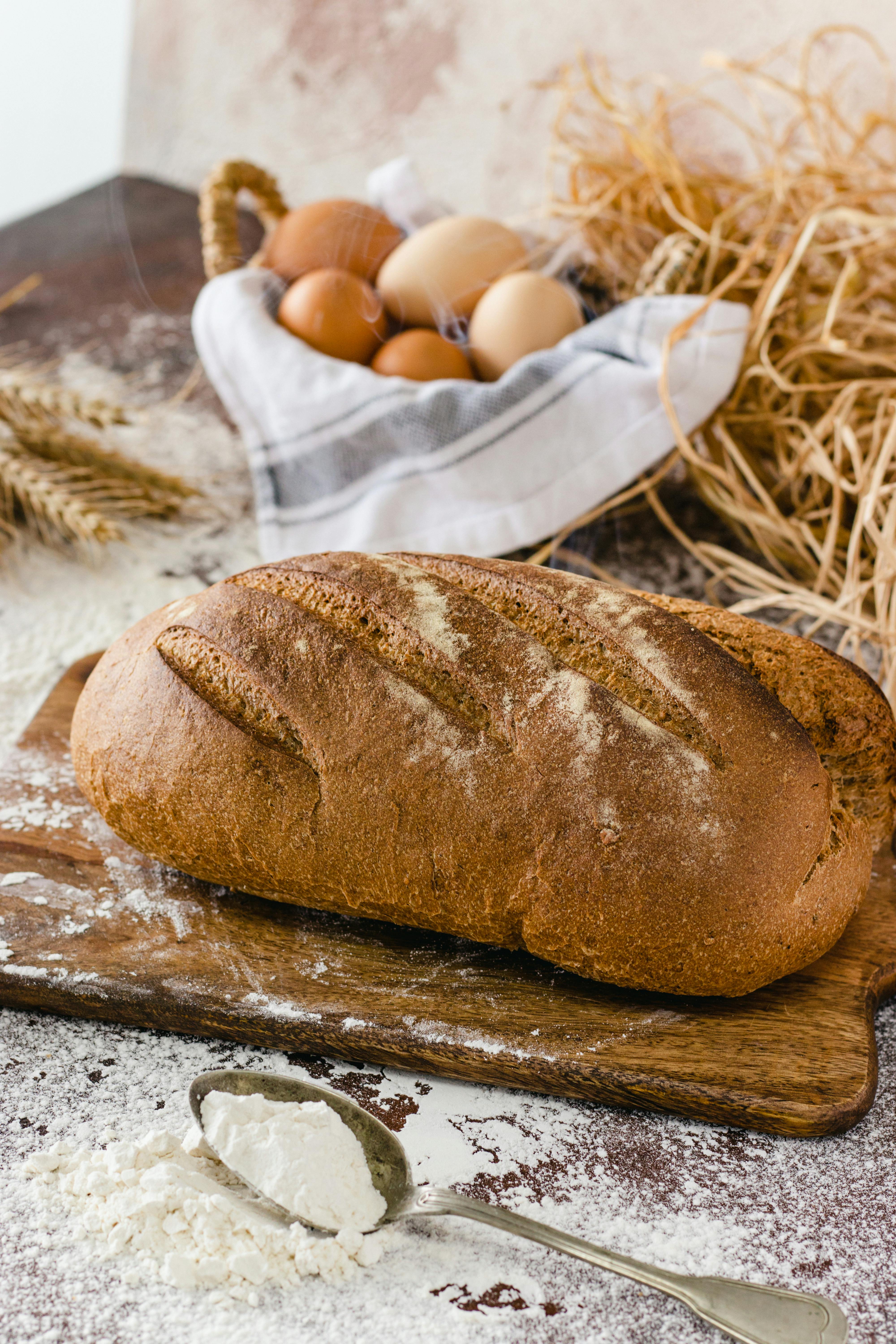 Rustic whole wheat bread with eggs and wheat on a wooden board, showcasing artisanal baking.
