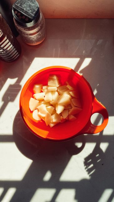 A bowl of soft, peeled apple chunks simmered until tender, dusted with cinnamon, with a slotted spoon resting beside the bowl.